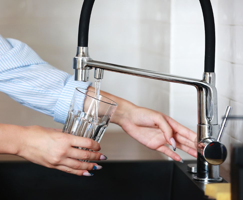 A person filling a glass with tap water, which contains Fluoride.