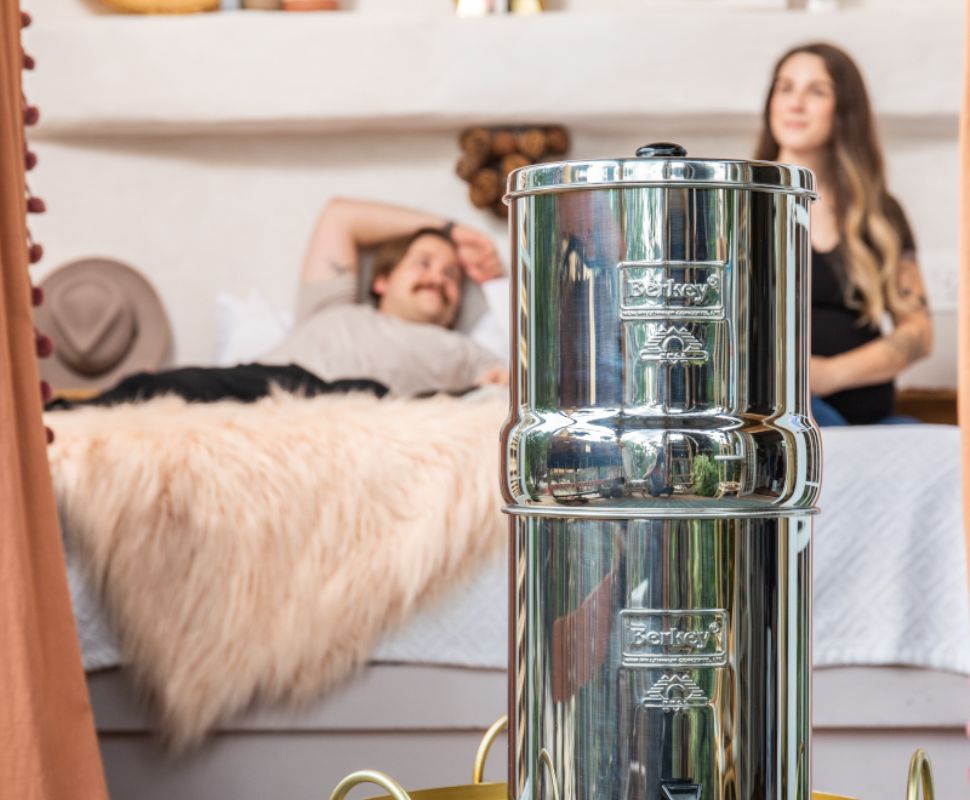 A Berkey Filter in the foreground with a family in the back, all settled at home.