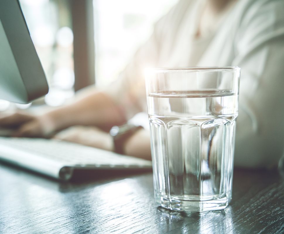 A person at an office computer, with a glass of water in the foreground.